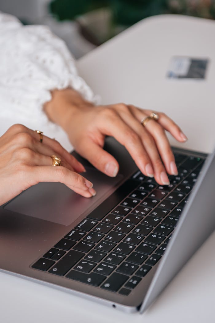 services-01 Hands of a woman typing on a laptop keyboard indoors, showcasing rings and fashion.